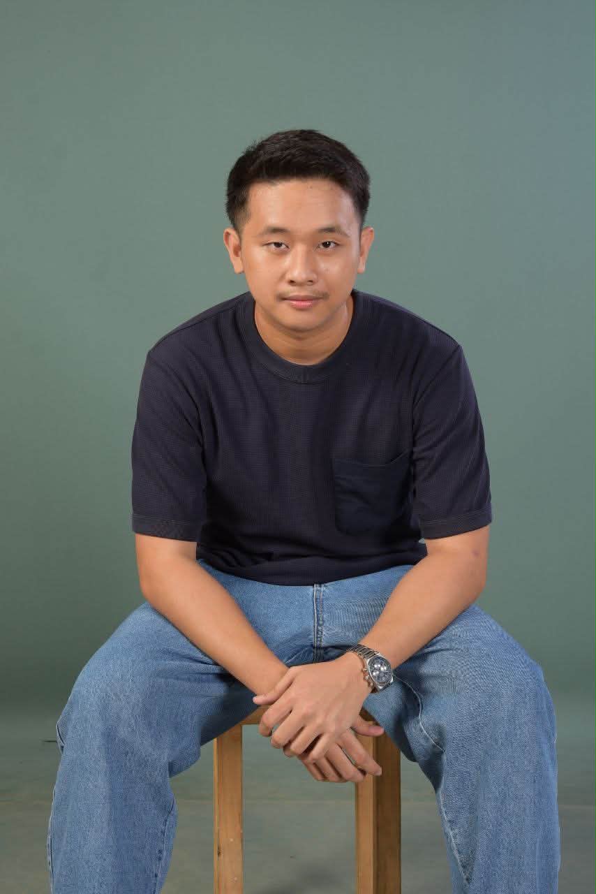 Caleb T. Lopez, seated portrait against a sage-green studio backdrop.